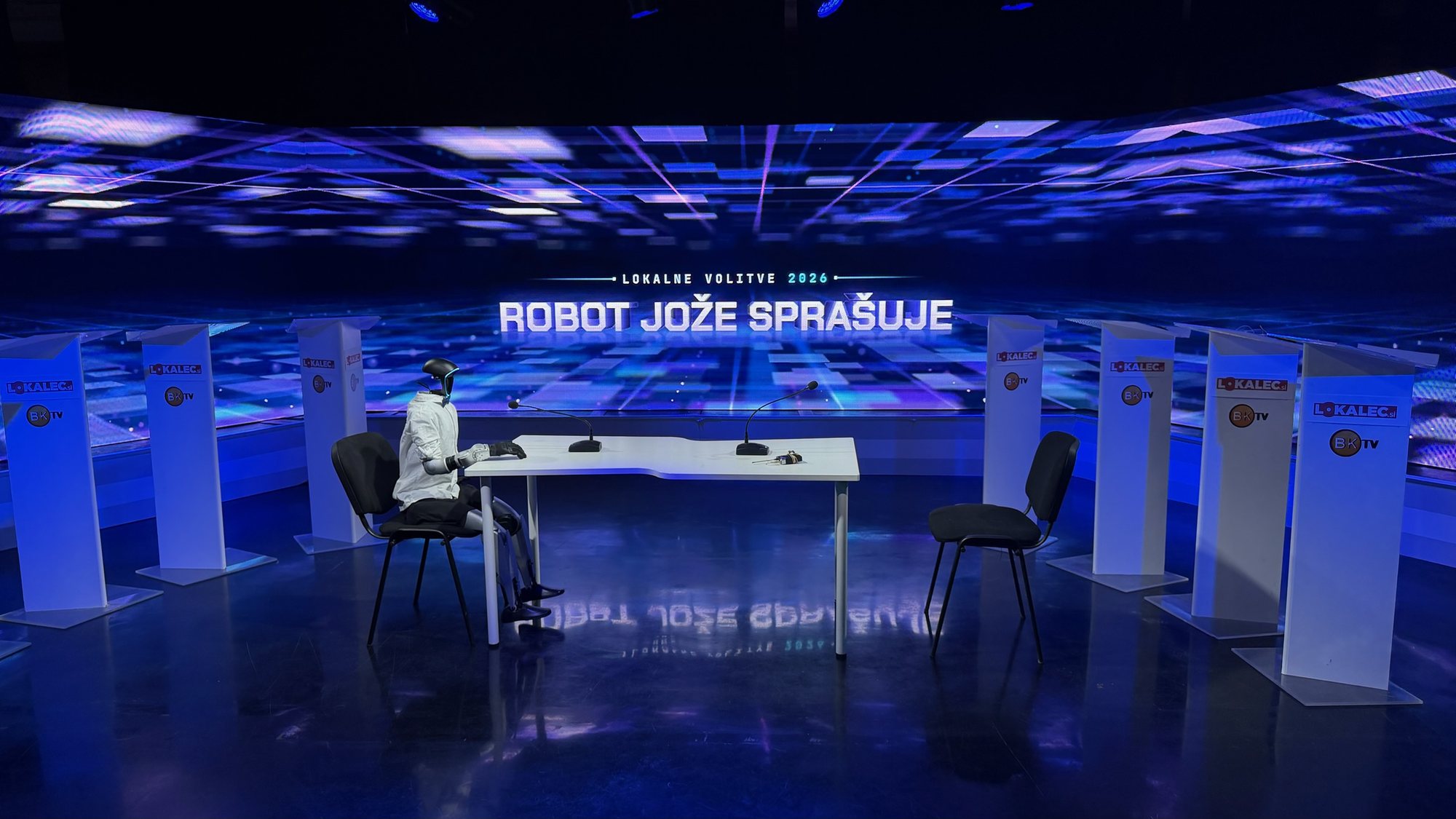 Humanoid robot Jože at the desk in the BK TV studio, set of Lokalne volitve 2026: Robot Jože sprašuje
