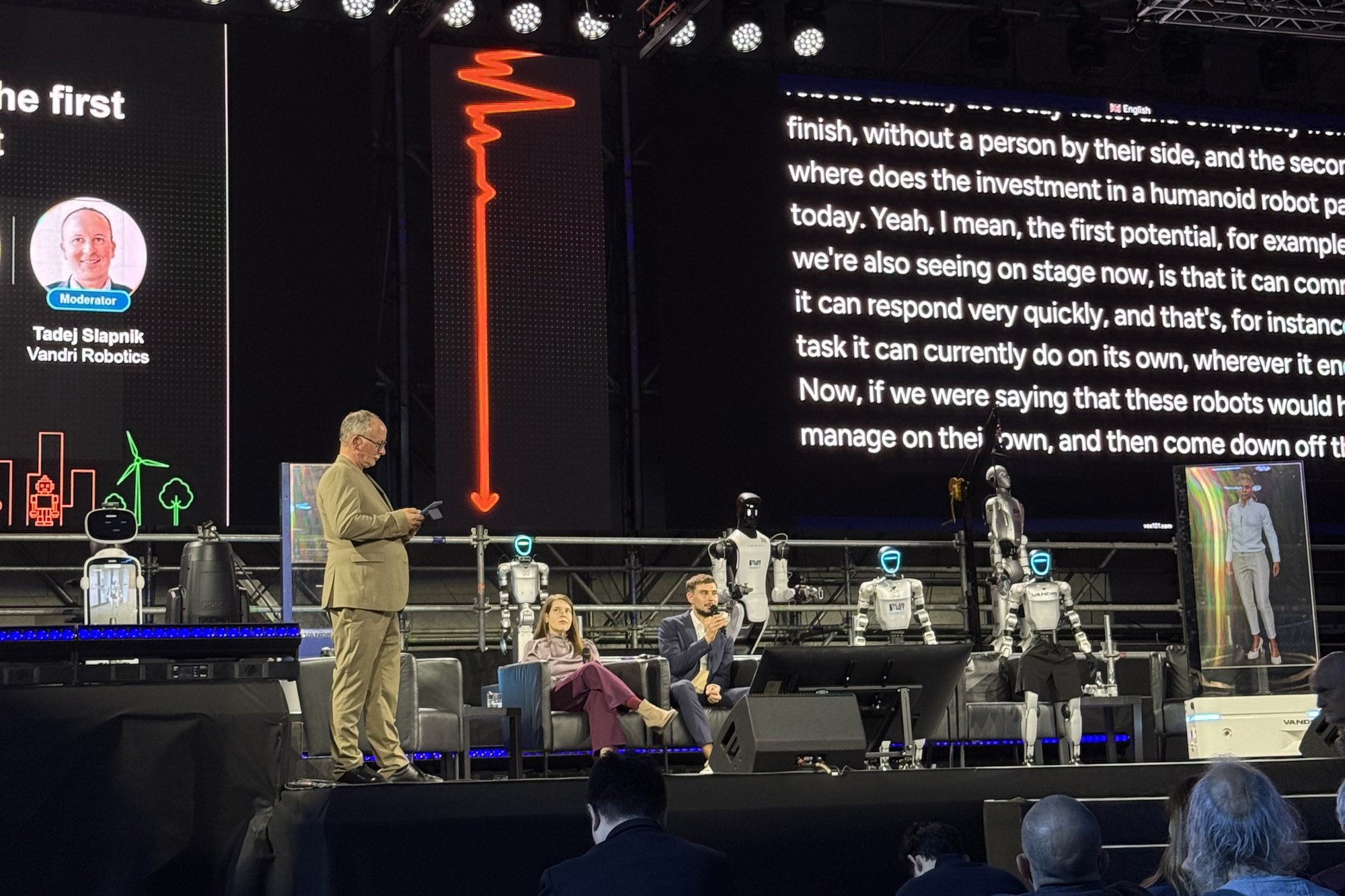 Tadej Slapnik moderating a panel with humanoid robots and Lumen on stage at IMPULZ 2026